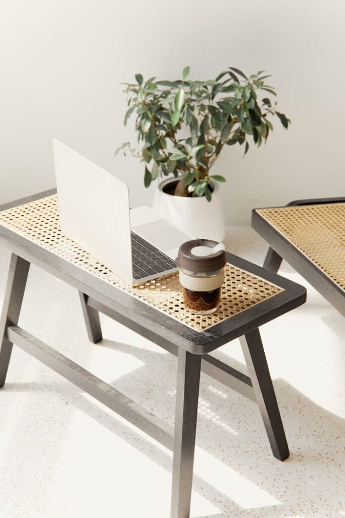A sleek minimalist setting featuring a laptop and reusable coffee cup on a woven bench.